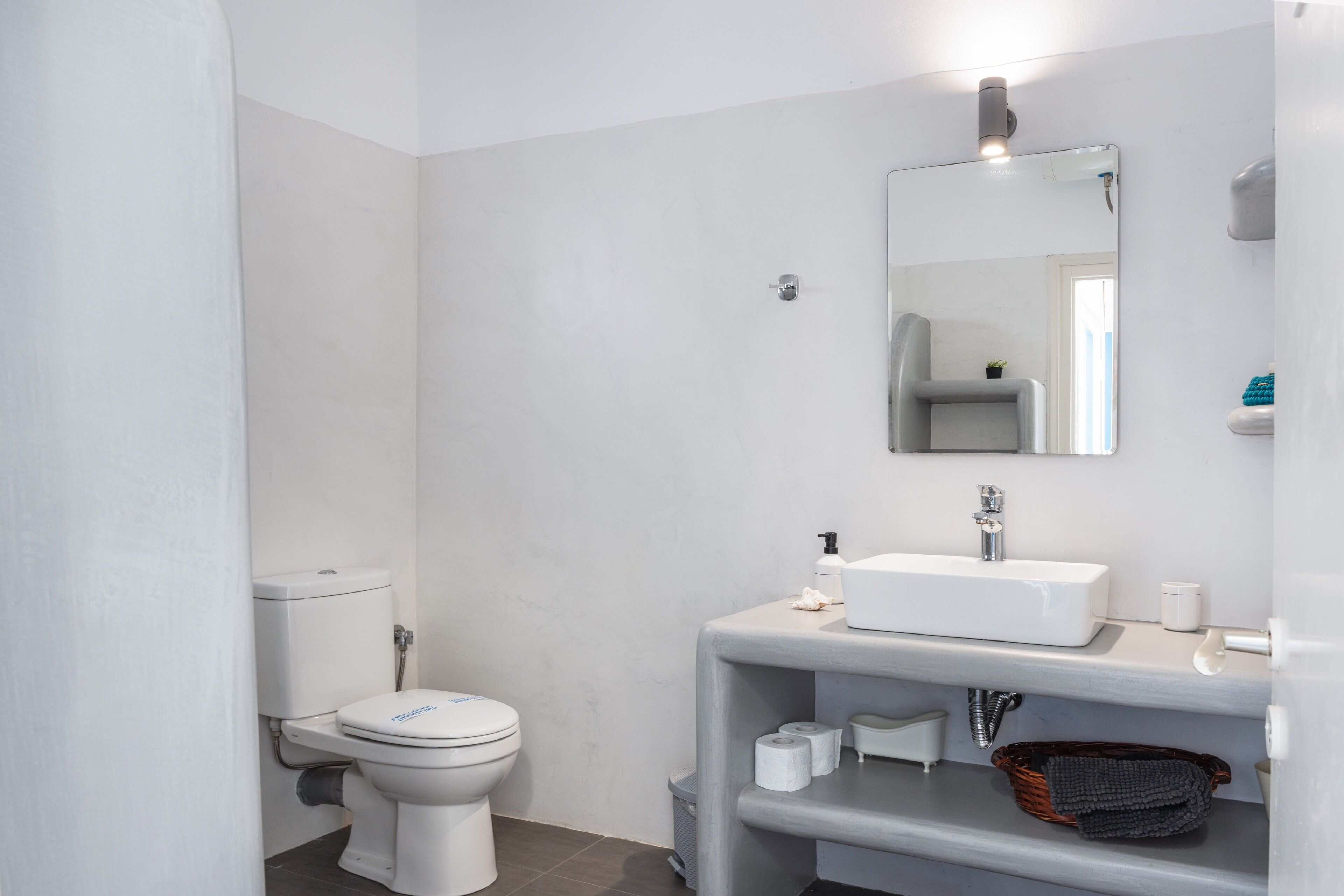 Un baño moderno con inodoro, lavamanos, espejo y estantes de almacenamiento.