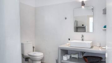 Un baño moderno con inodoro, lavamanos, espejo y estantes de almacenamiento.