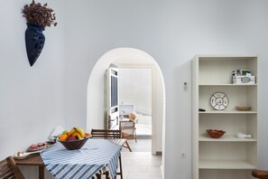 A dining area with a table set for two, a bowl of fruit, and a white shelf with various items.