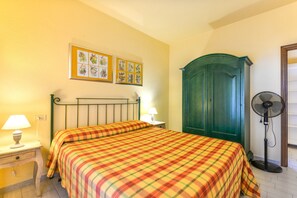 A bedroom with a bed, two wall-mounted lamps, a green wardrobe, and a standing fan.