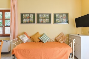 Une chambre à coucher avec un lit, des oreillers, une télévision, une commode et trois tableaux représentant des motifs floraux, accrochés au mur.