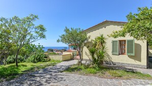 Une maison avec un chemin de pierre, des volets verts et une vue sur la mer.