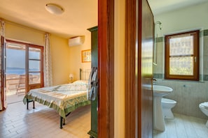A bedroom with a bed, a fan, a window, and a bathroom with a toilet and sink. - Apartment 'Cinciarella  Casa Vai' with Sea View, Wi-Fi and Air Conditioning (Marciana Località Zanca)