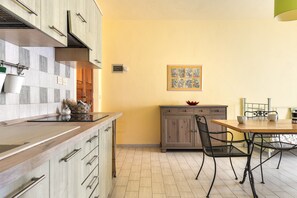A kitchen with a wooden countertop, cabinets, a dining table with chairs, and a wall-mounted picture.