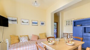 A room with a bed, a dining table with chairs, a TV mounted on the wall, and framed pictures.