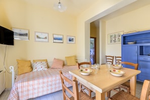 Une pièce comprenant un lit, une table à manger avec des chaises, un téléviseur fixé au mur et des tableaux encadrés.