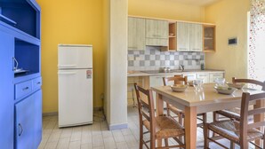 A compact kitchen with a refrigerator, wooden cabinets, and a dining table with chairs.