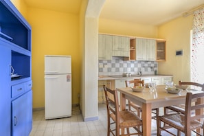 Une cuisine compacte équipée d’un réfrigérateur, de meubles de rangement en bois et d’une table à manger avec des chaises.