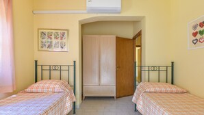 A room with two beds, a wardrobe, an air conditioner, and a framed picture on the wall.