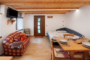 A cozy room with a sofa, a bed, a dining table set for two, and a television mounted on the wall.