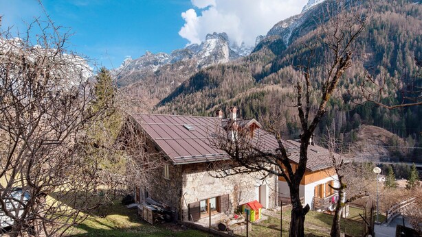 Un edificio de piedra con techo metálico, rodeado de árboles y montañas.