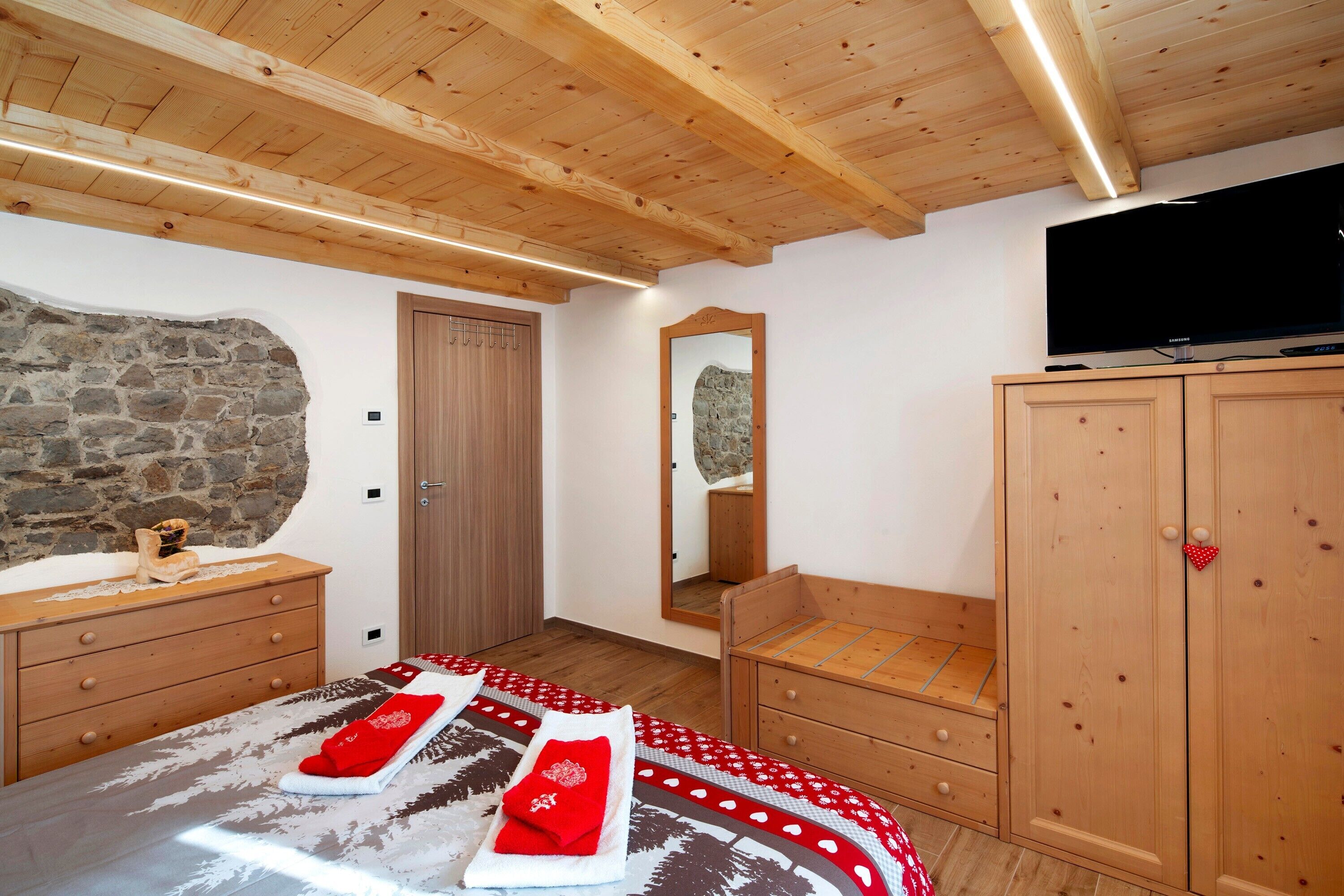 Een slaapkamer met een houten plafond, een stenen muur, een houten garderobe en een televisietoestel.