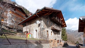 Un edificio de piedra con techo inclinado, un balcón y una pequeña estructura roja cerca.