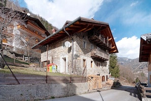 A stone building with a sloped roof, a balcony, and a small red structure nearby.
