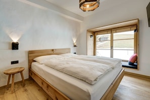 Un dormitorio con cama de madera, dos lámparas de pared, un taburete pequeño y una ventana con vistas al exterior.