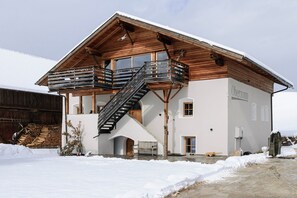 Een houten chalet met een balkon, een trap en een met sneeuw bedekte grond.