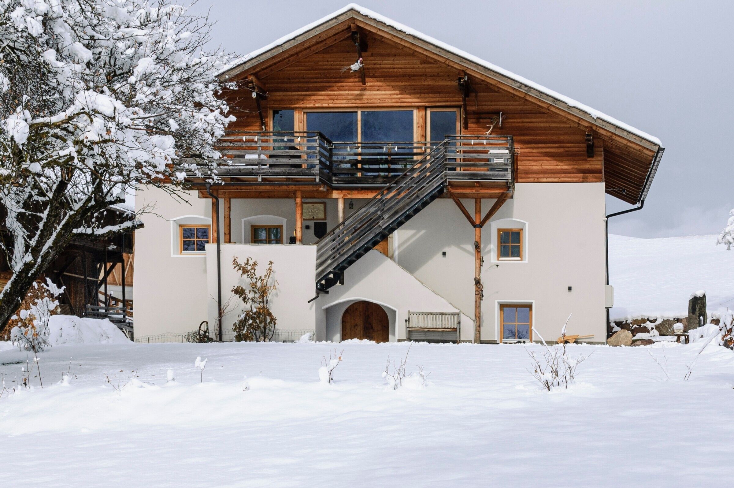 Ein zweistöckiges Holzhaus mit Balkon und Treppe, vor einer verschneiten Landschaft.