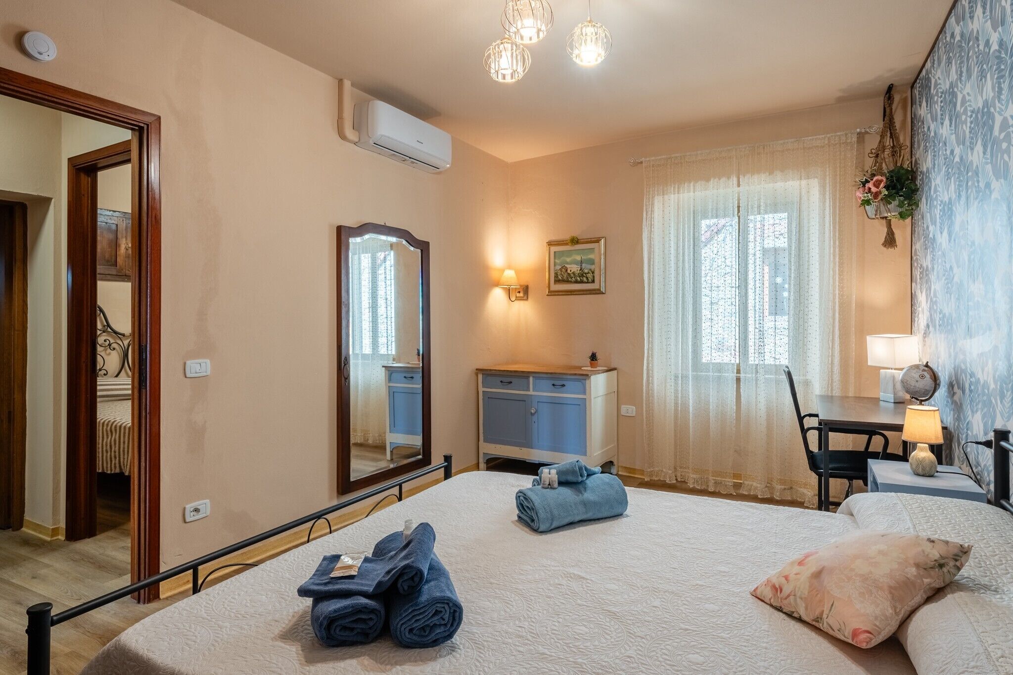 Une chambre à coucher comprenant un lit, une commode, un miroir, un bureau avec une lampe et une fenêtre avec des rideaux.