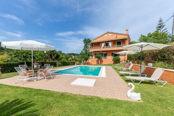 Área de piscina com espreguiçadeiras, mesa e guarda-sóis.