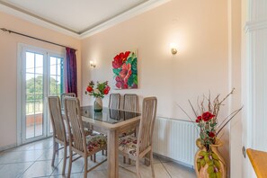 Een eetgedeelte met een glazen tafel, stoelen en een schilderij aan de muur.