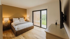 Ein Schlafzimmer mit einem Bett, Nachttischlampen, einem Fernseher und einer Schiebetür zu einem Balkon.