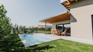 Ein modernes Haus mit Swimmingpool, Sitzgelegenheiten im Freien und einer überdachten Terrasse.
