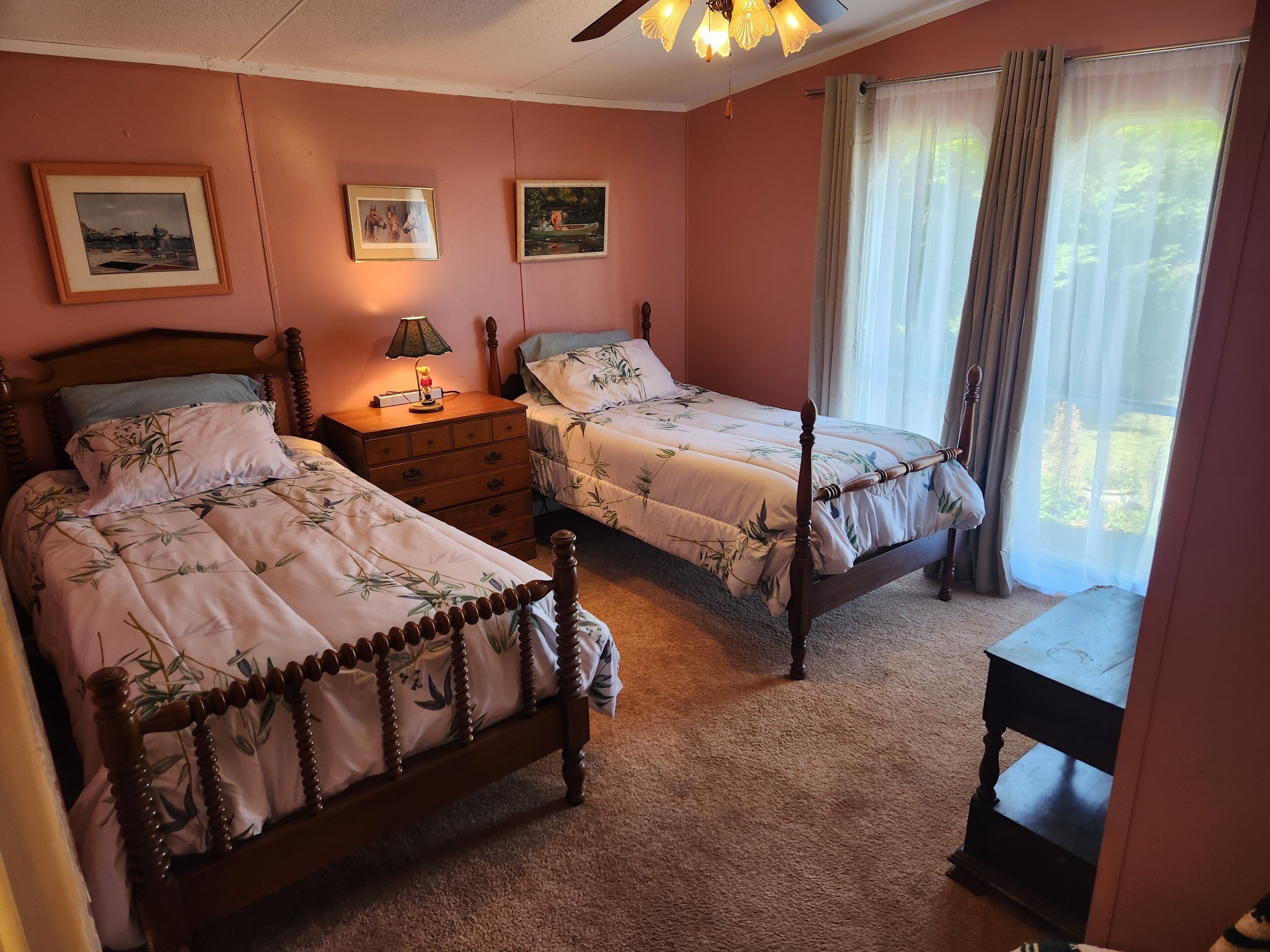 A bedroom with two wooden beds, a nightstand with a lamp, and a window with curtains.