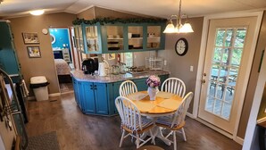A kitchen with teal cabinets, a dining area with white chairs, and a view of the outdoors through a glass door.