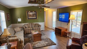 A living room with a sofa, armchairs, a coffee table, a television, and a ceiling fan.