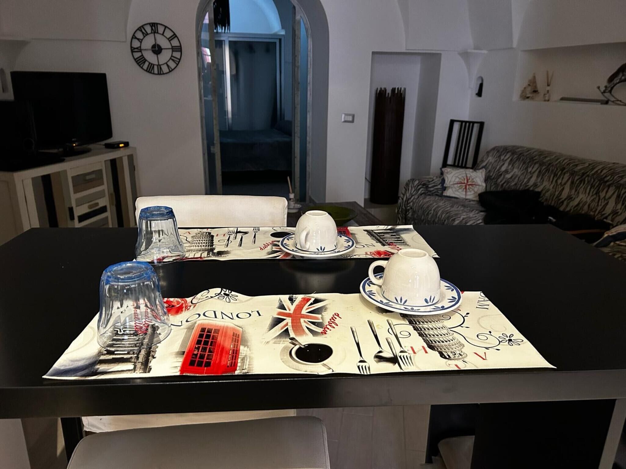 Mesa con mantel individual con tema de Londres, una taza blanca, un vaso y cubiertos.