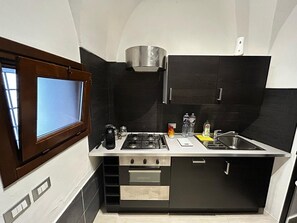 Una cucina compatta con fornelli a gas, forno e una finestra con persiane.