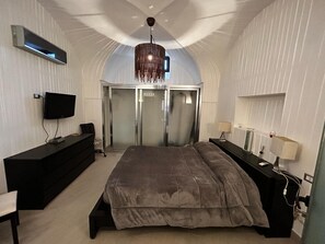 Ein Schlafzimmer mit Bett, Fernseher, Schreibtisch, Kleiderschrank und einer Chandelier.