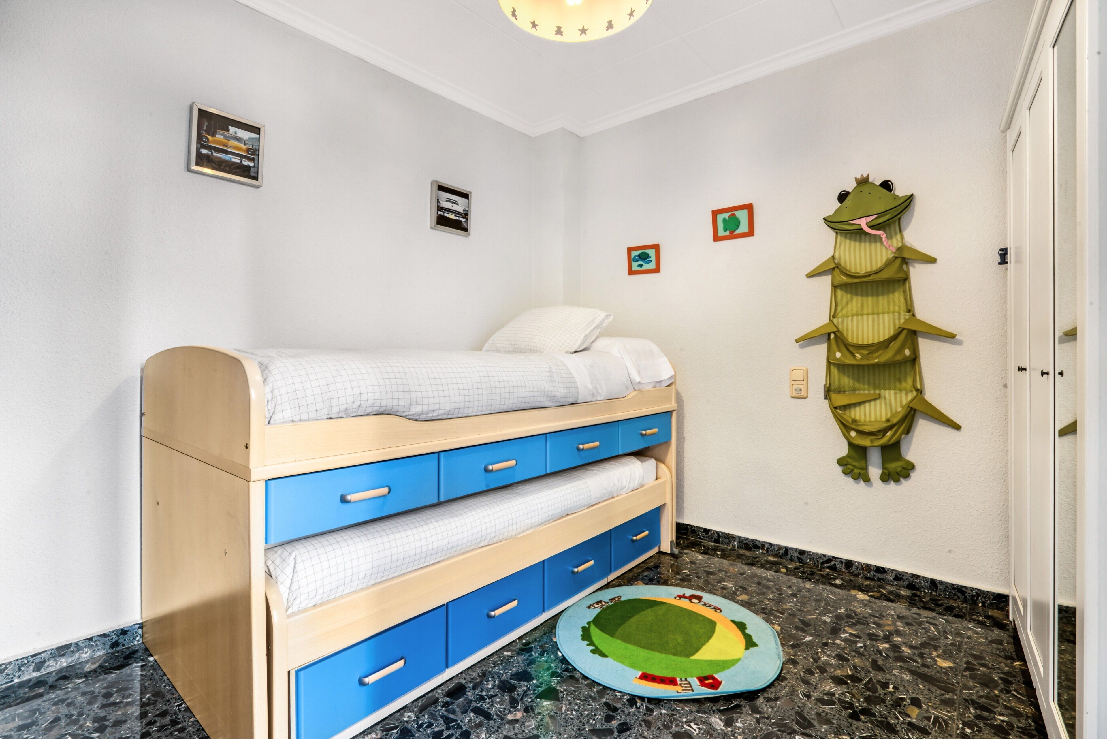 Een kinderstapelbed met lades, een kleedje en een wanddecoratie.