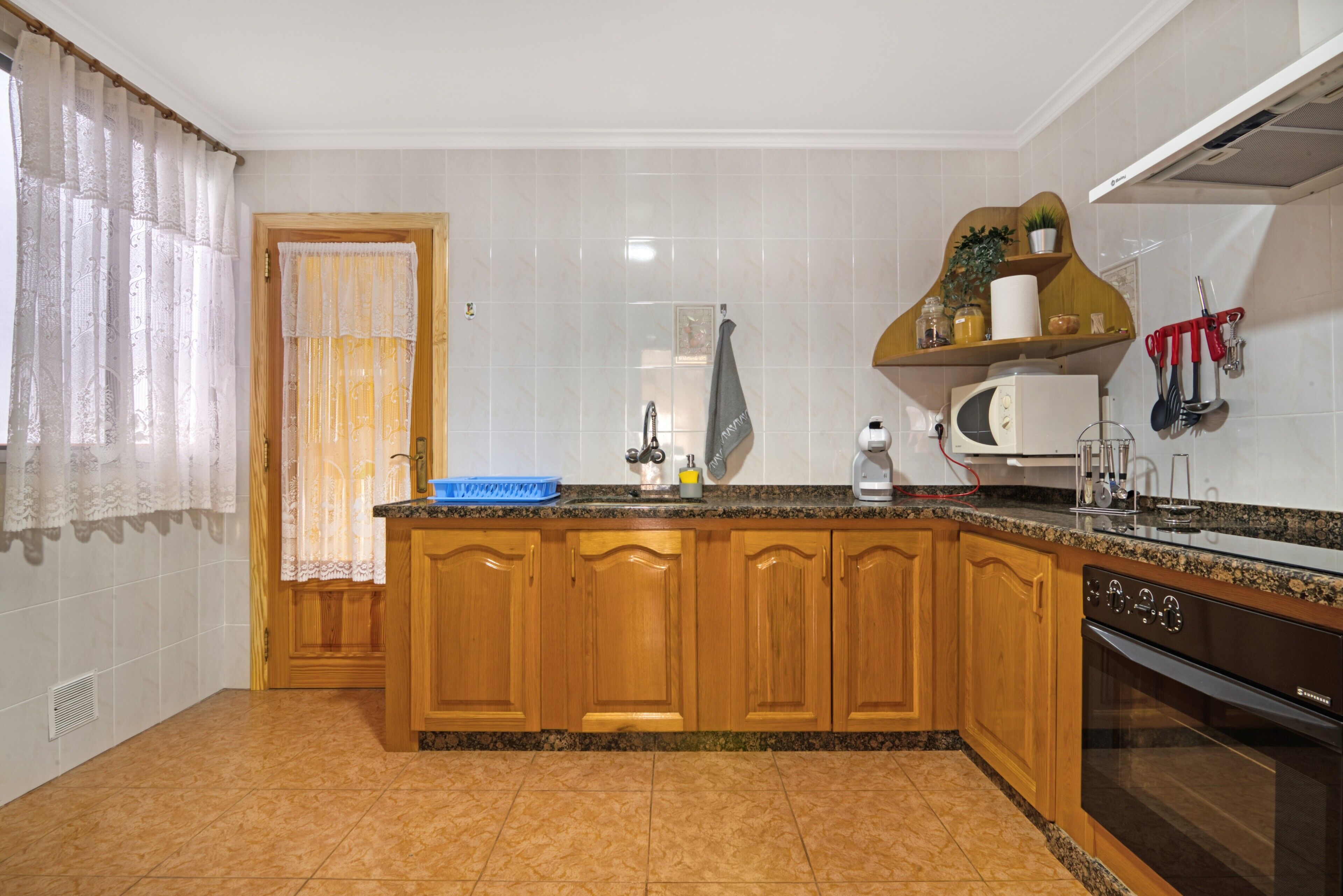 Una cocina con armarios de madera, microondas, horno y lavamanos.