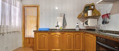 Una cocina con armarios de madera, microondas, horno y lavamanos.