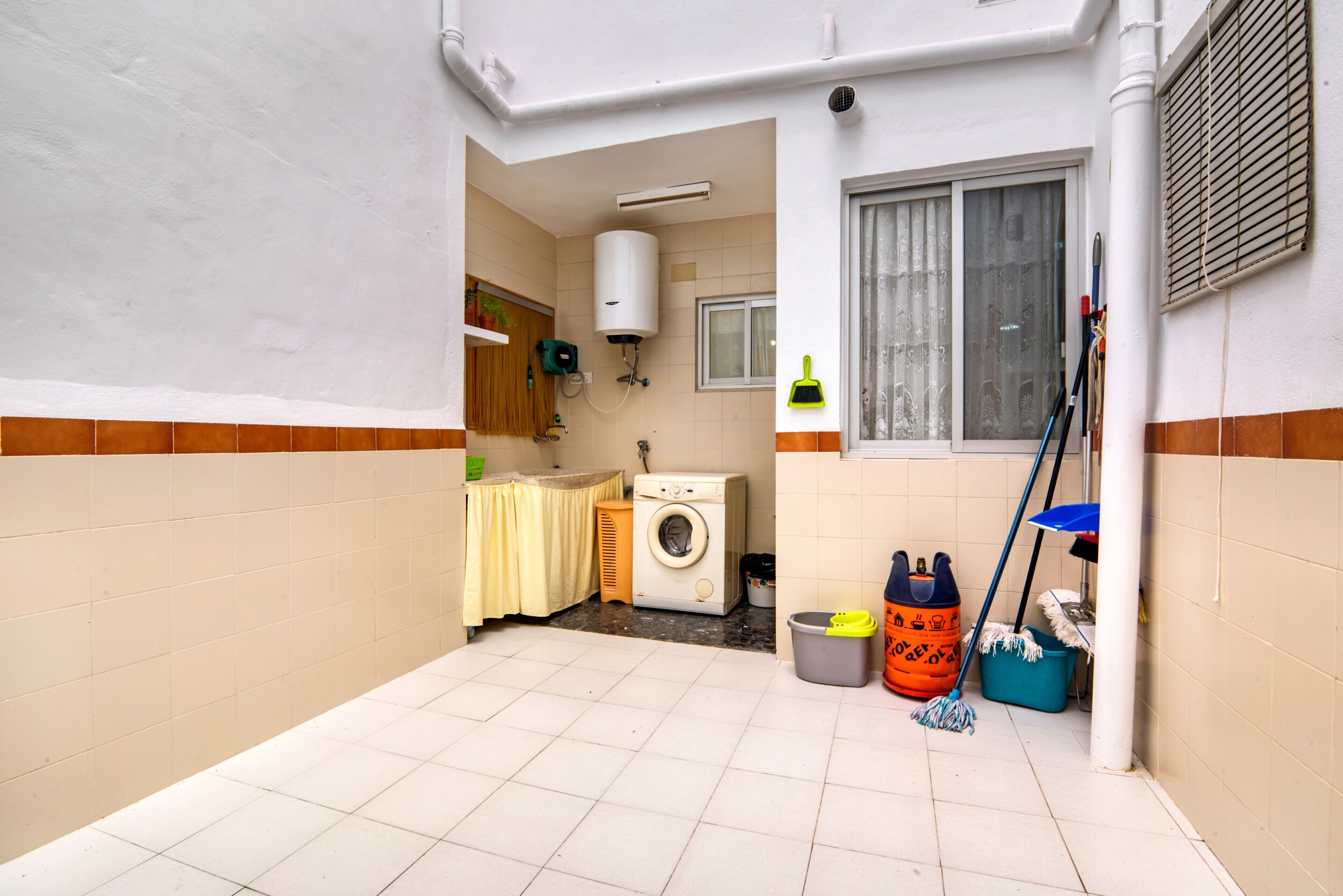 Une buanderie équipée d’un lave-linge, d’un radiateur, d’une fenêtre et de produits de nettoyage.