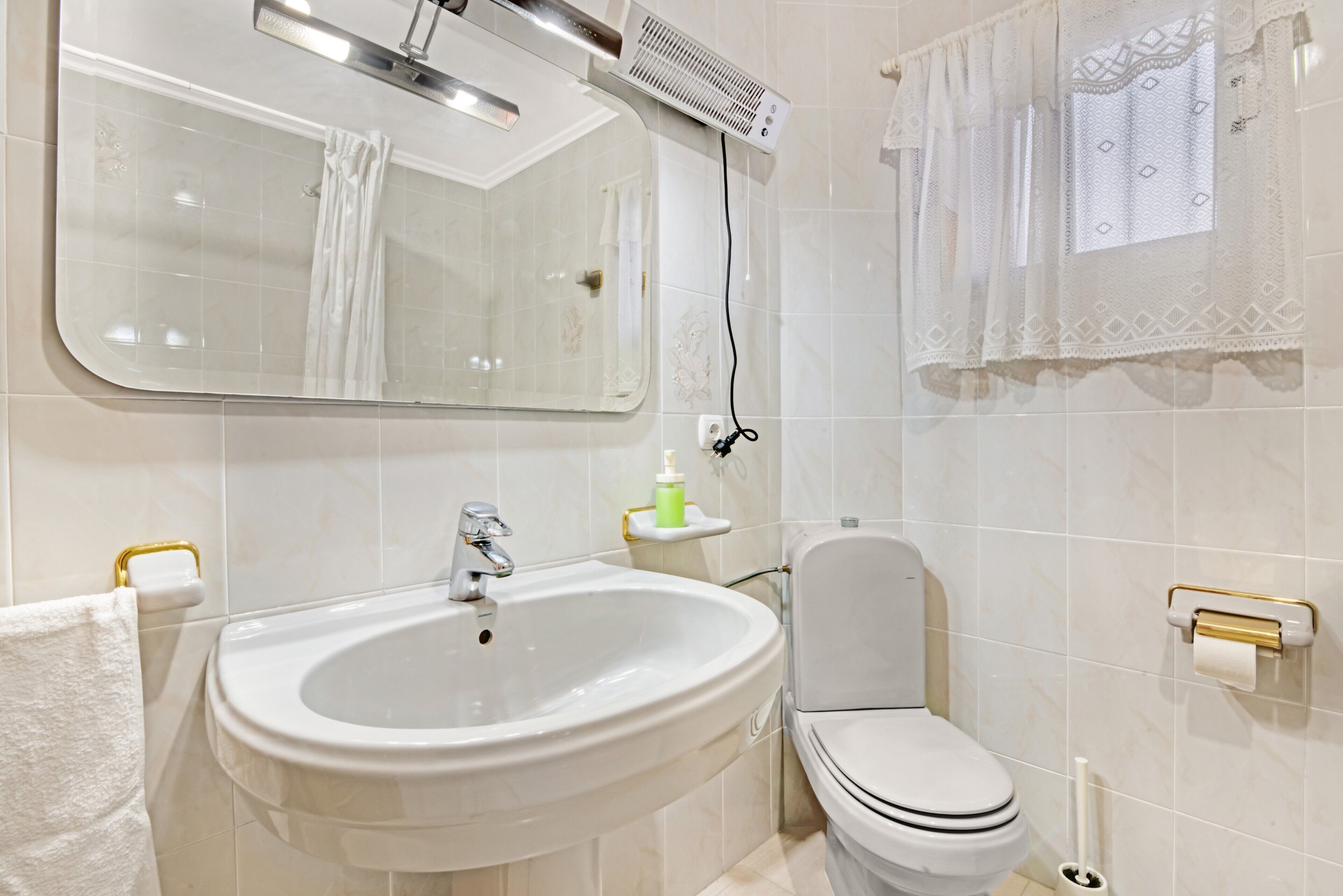 Un baño con lavamanos, espejo, inodoro y toallero.