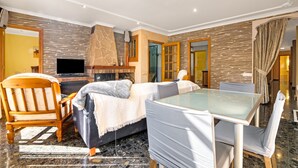 Ein modernes Hotelzimmer mit Kamin aus Naturstein, einem Flachbildfernseher, einer Couch, einem Esstisch mit Stühlen und einem großen Spiegel.