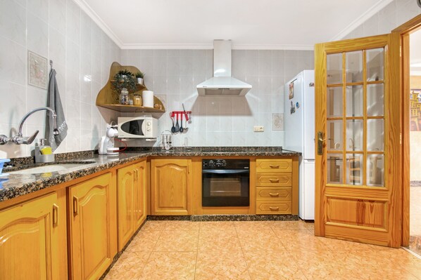 A kitchen with wooden cabinets, a built-in oven, a microwave, and a refrigerator.