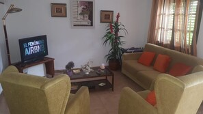 A living room with a sofa, armchairs, a coffee table, a television, and a potted plant.