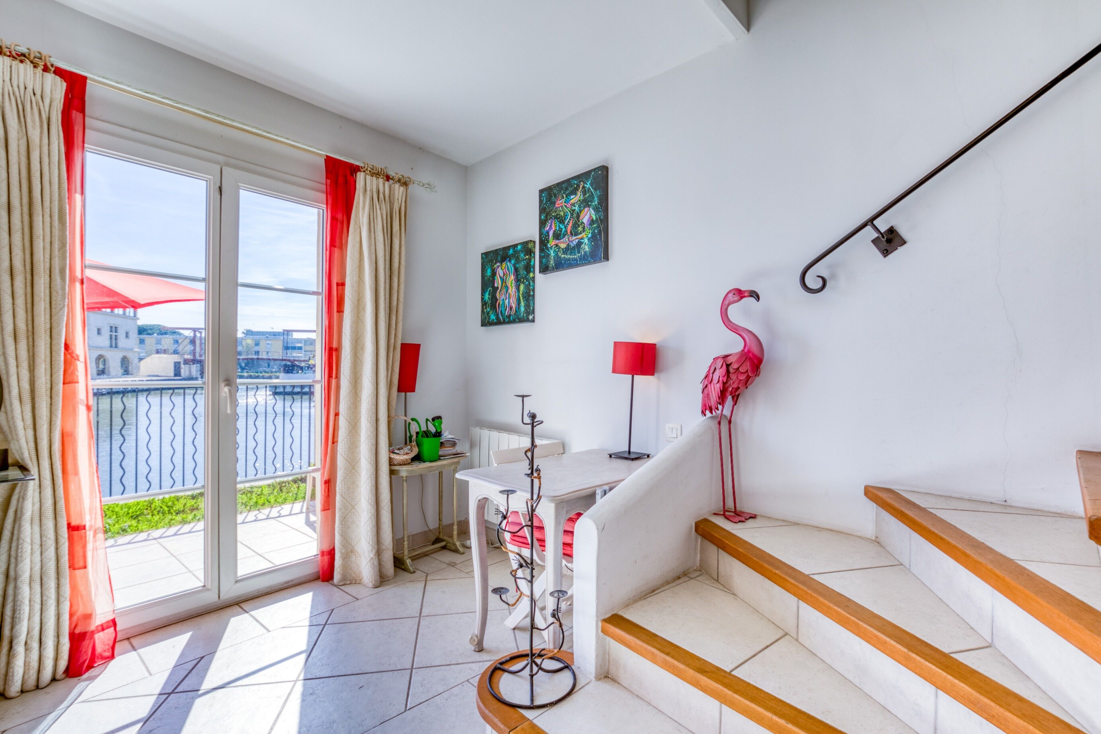 A room with a balcony, a table with a chair, a staircase, and two wall-mounted lamps.