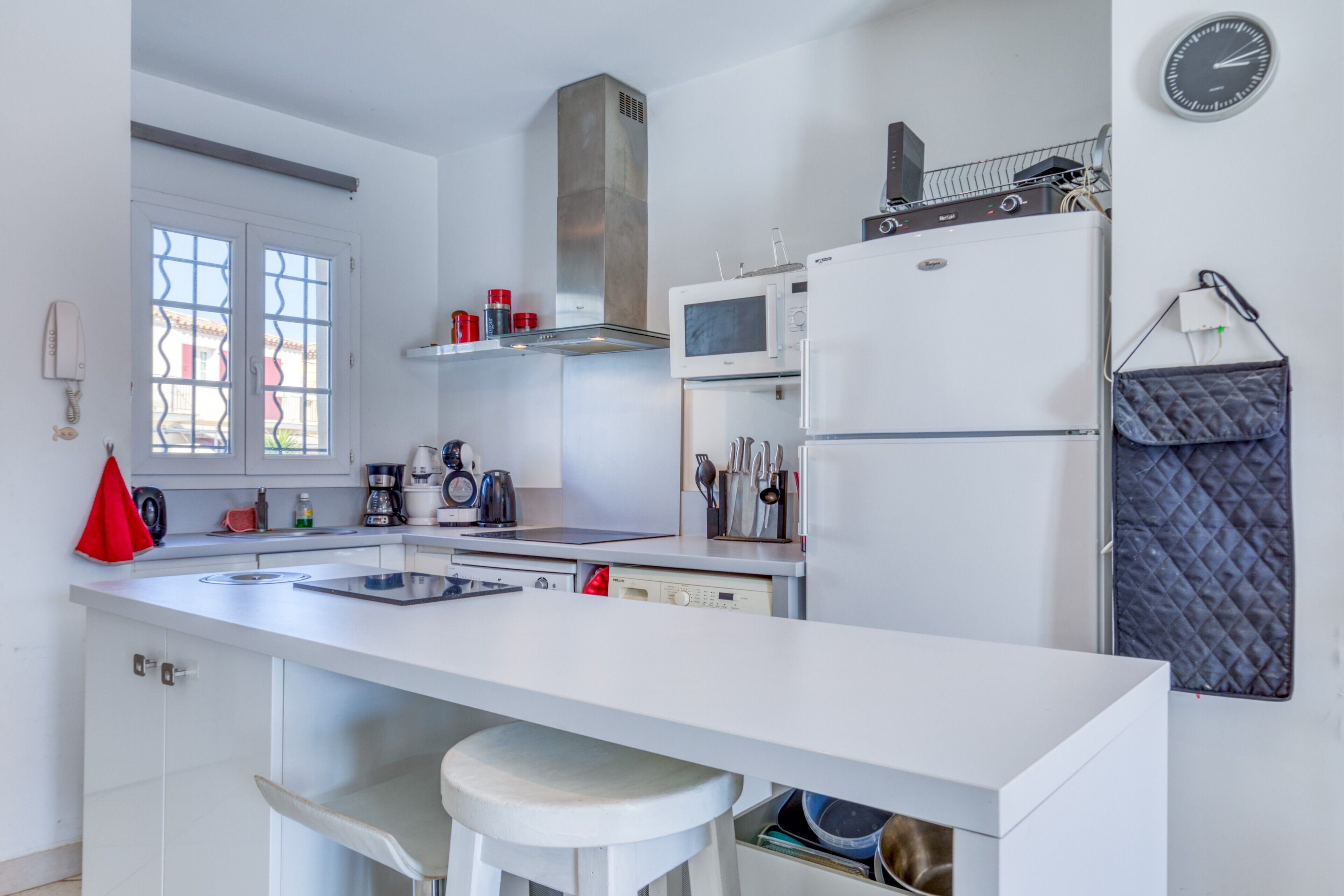 Une cuisine moderne avec un plan de travail blanc, des appareils en acier inoxydable et une grande fenêtre.