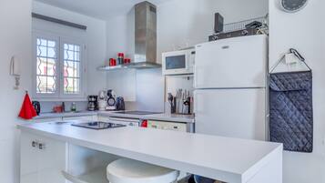 Une cuisine moderne avec un plan de travail blanc, des appareils en acier inoxydable et une grande fenêtre.