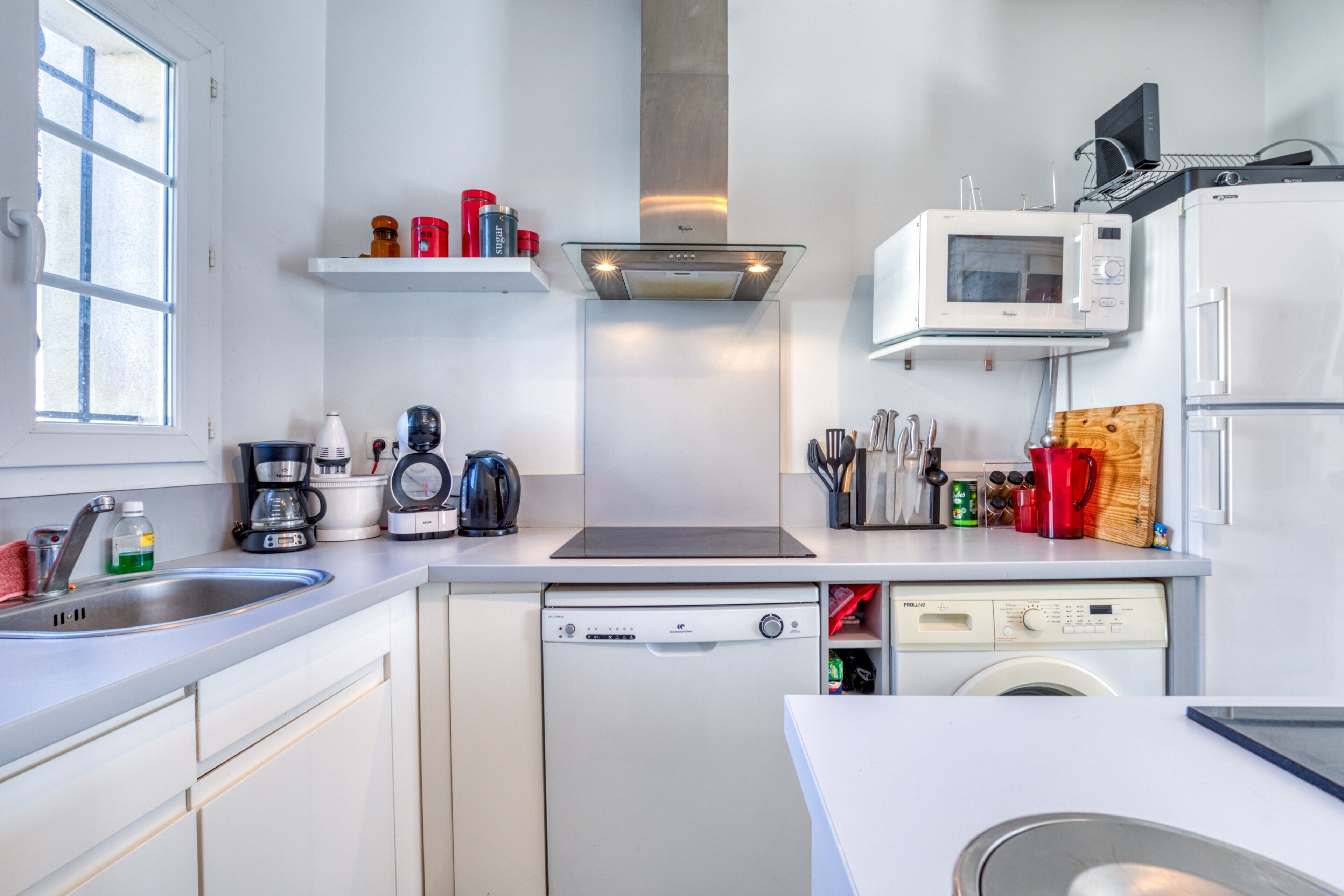 Een moderne keuken met een vaatwasser, magnetron en oven, een raam en een spoelbak.
