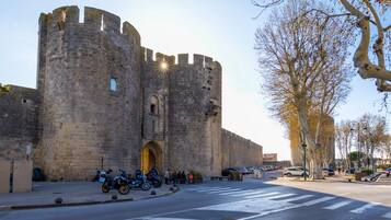 Un château de pierre historique, doté d’une grande entrée en arc de cercle, où sont garées des motos, et sous un ciel dégagé.
