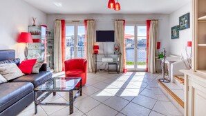 A modern living room with a sofa, red chair, glass coffee table, and a TV. - 'Petite Maison Aigues Mortes' with Sea View, Shared Pool and Wi-Fi (Aigues-Mortes)
