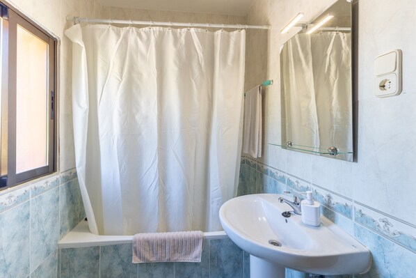 A bathroom with a bathtub, a sink, a mirror, and a window.