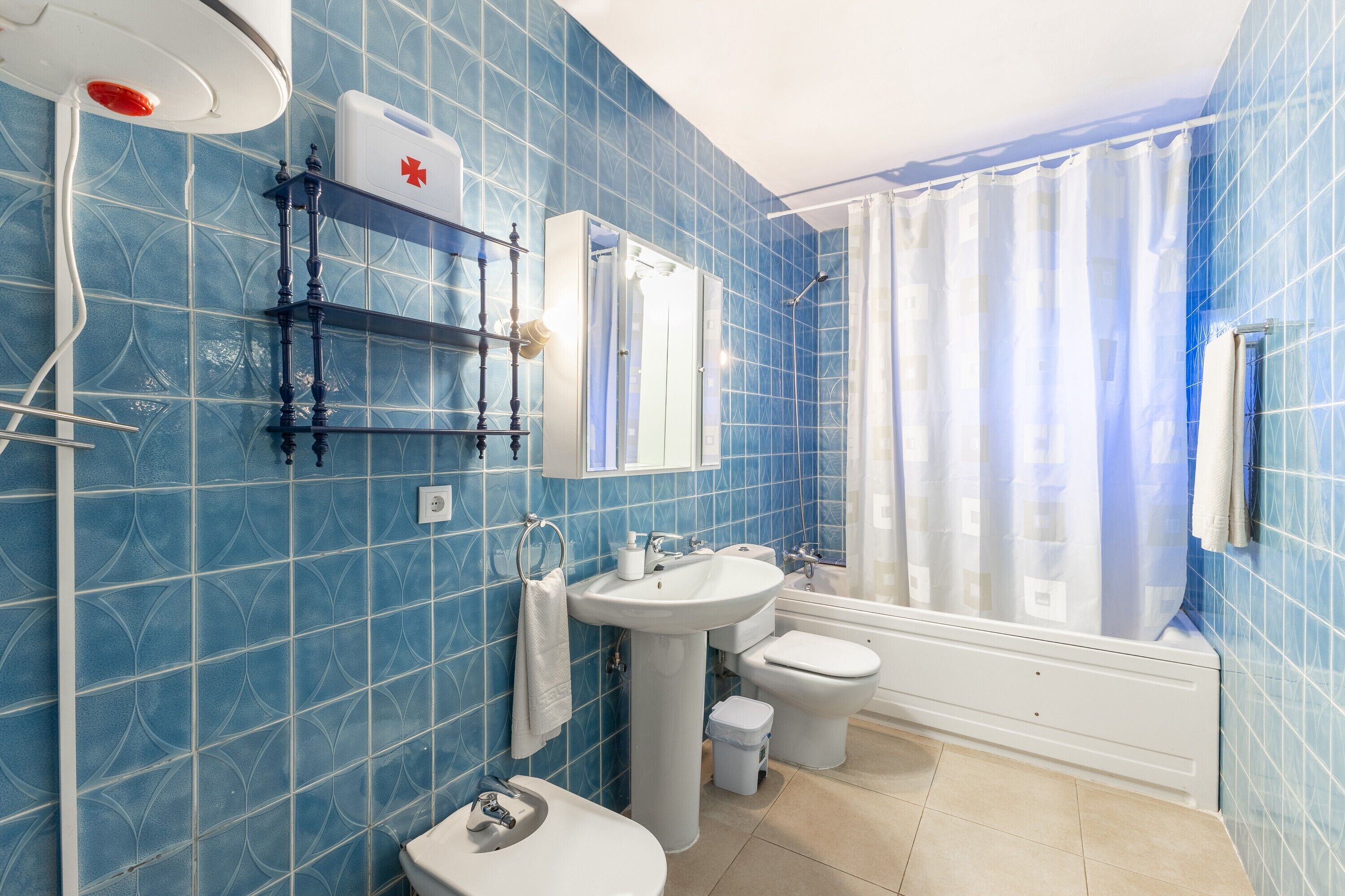 A bathroom with blue tiles, a sink, a toilet, a bathtub, and a shower curtain.