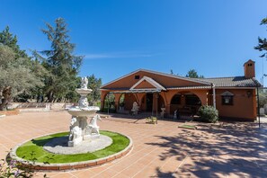 A building with a tiled patio, a fountain with a statue, and a covered area with arches.