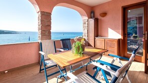 Un balcón con mesa y sillas de madera, un muro de piedra y vista al mar.